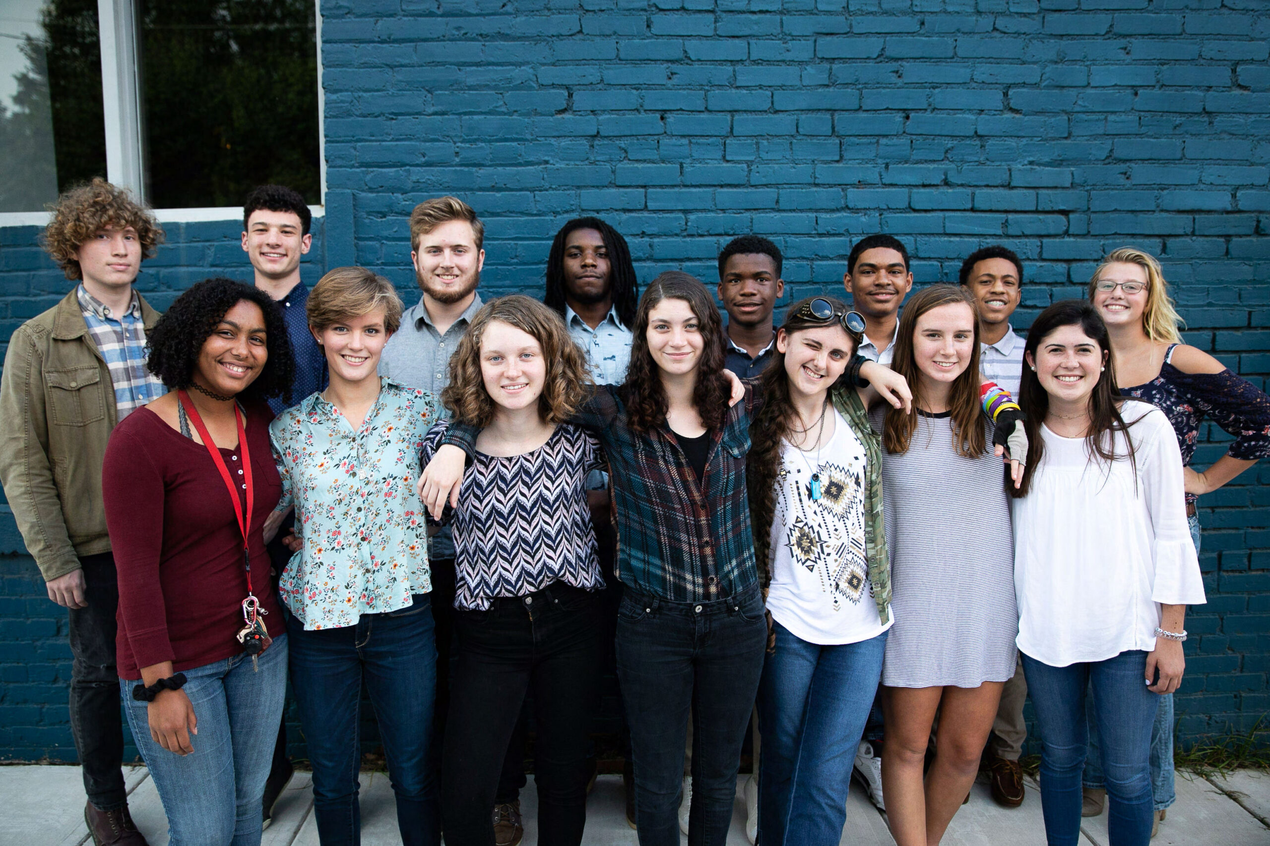 District C students smiling brightly and standing in front of a blue brick wall.